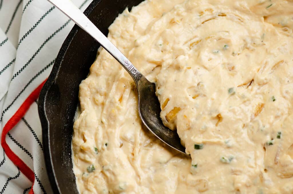 smoked caramelized onion dip scooped from cast iron pan with spoon