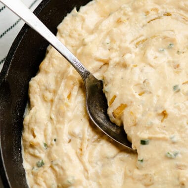 smoked caramelized onion dip scooped from cast iron pan with spoon