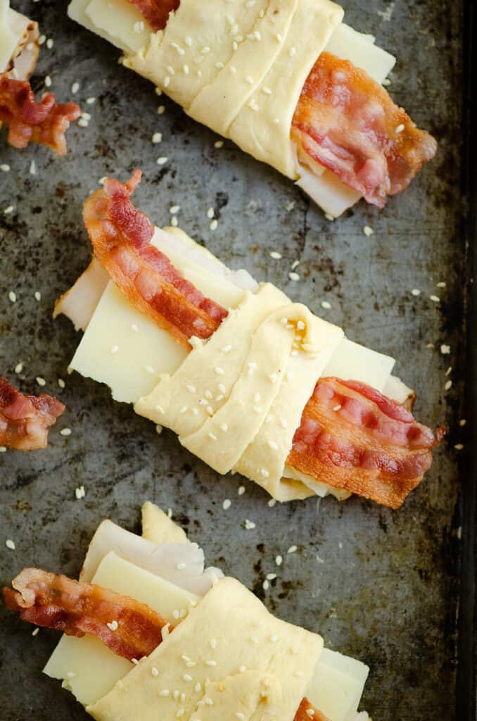 turkey bacon swiss crescent rolls topped with sesame seeds on sheet pan