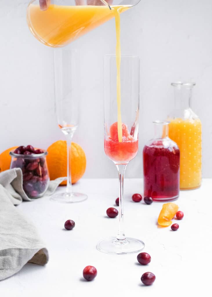 orange juice poured into mimosa glass with cranberry juice
