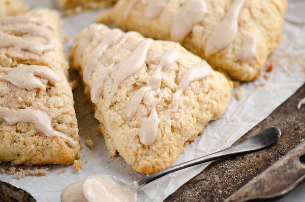 glazed cinnamon scones on parchment with spoonful of frosting