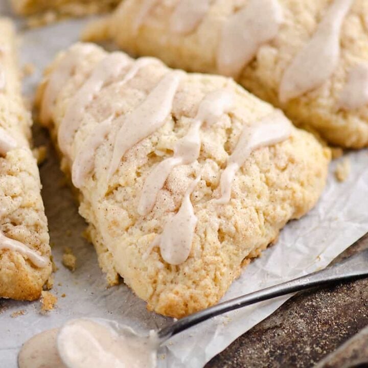 glazed cinnamon scones on parchment with spoonful of frosting