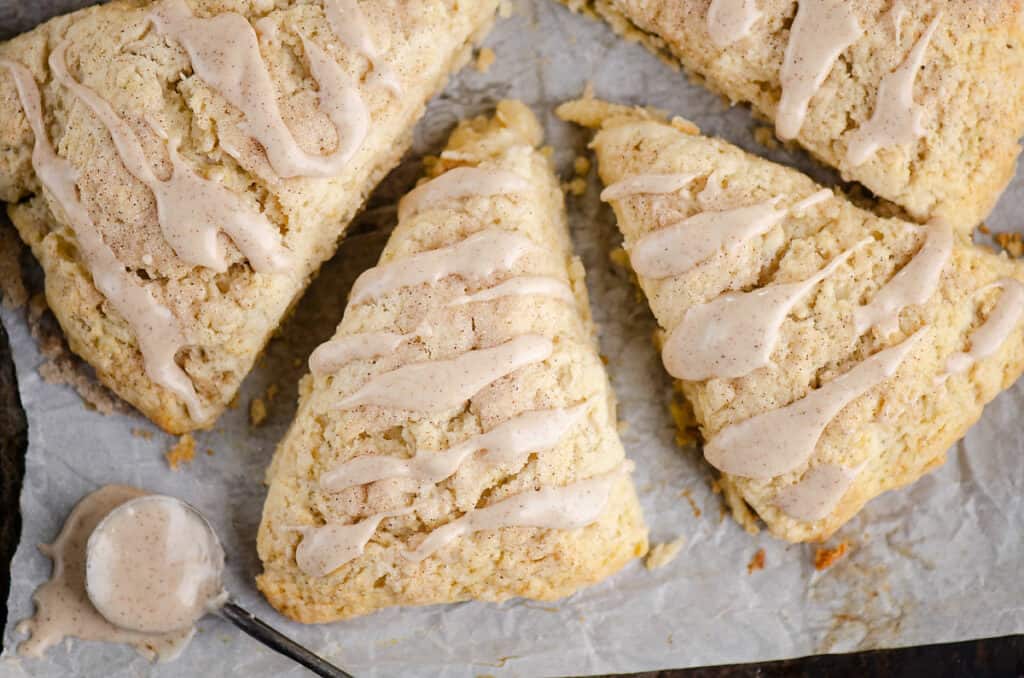 cinnamon scones on parchment with spoonful of glaze