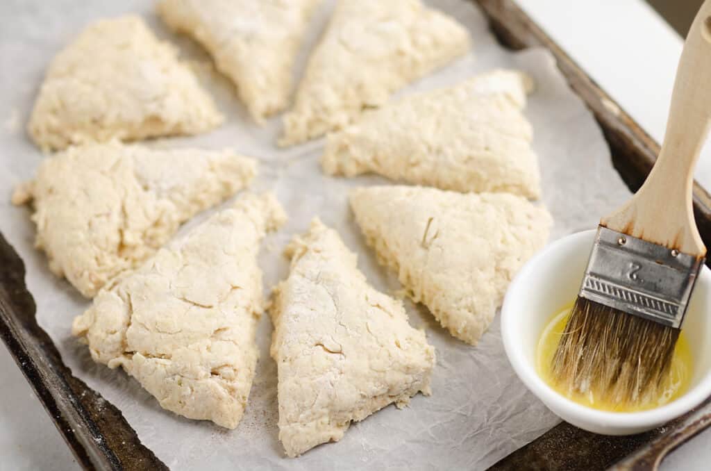 cinnamon scones on parchment lined baking sheet with bowl of melted butter