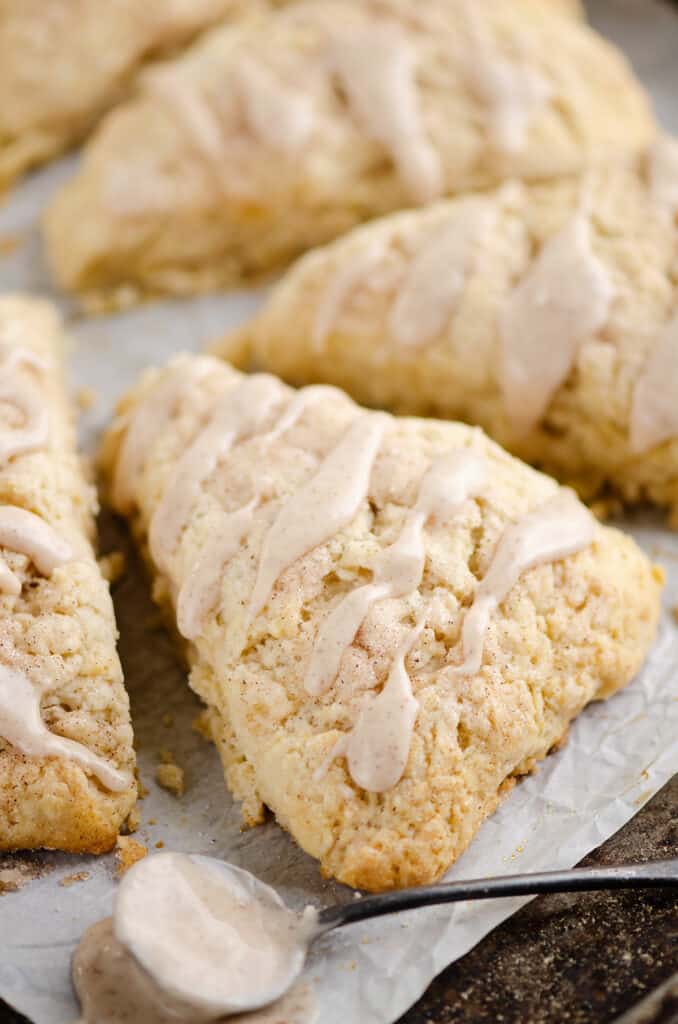 glazed cinnamon scone on parchment with spoon of frosting