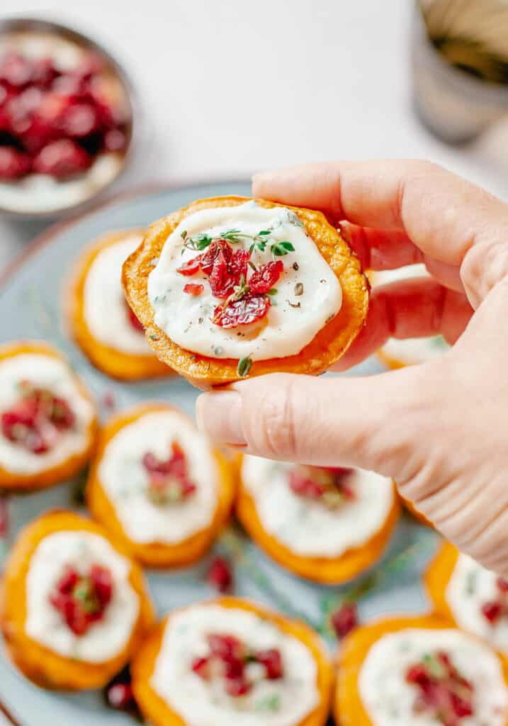 hand holding sweet potato bite topped with cranberries