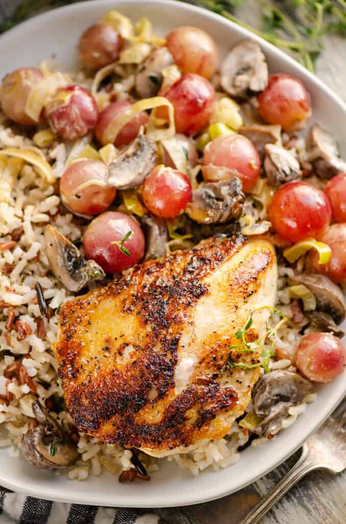 chicken breast on plate served with grapes, vegetables and grains