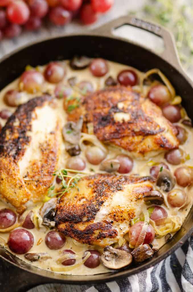cast iron skillet on table with chicken and grapes in cream sauce