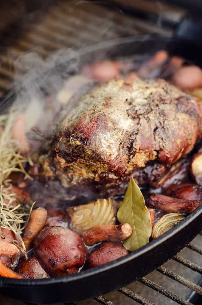 smoked pot roast and vegetables in cast iron pan on pellet grill