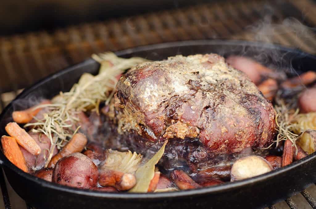 smoked pot roast and vegetables in cast iron pan on pellet grill