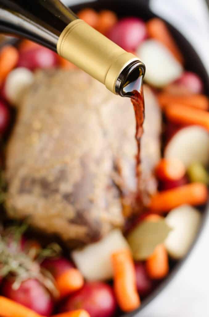 bottle of red wine pouring over pot roast nad vegetables