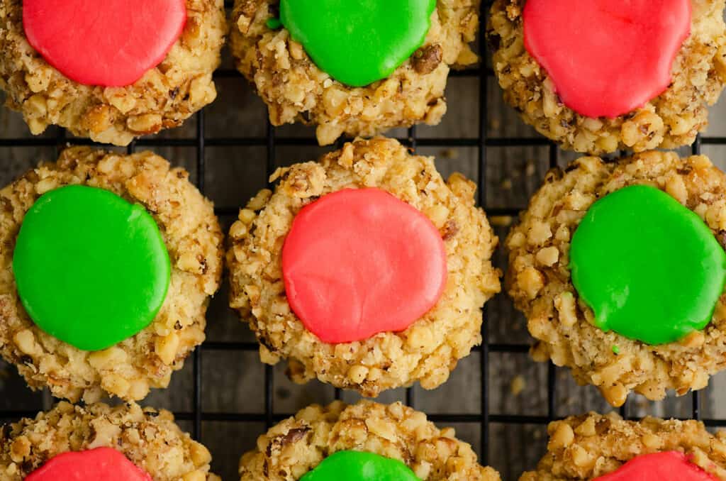 walnut thumbprint cookies with pink and green frosting on cooling rack