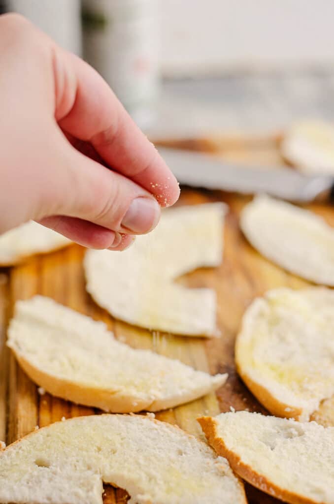 bagel slices being sprinkled with garlic salt