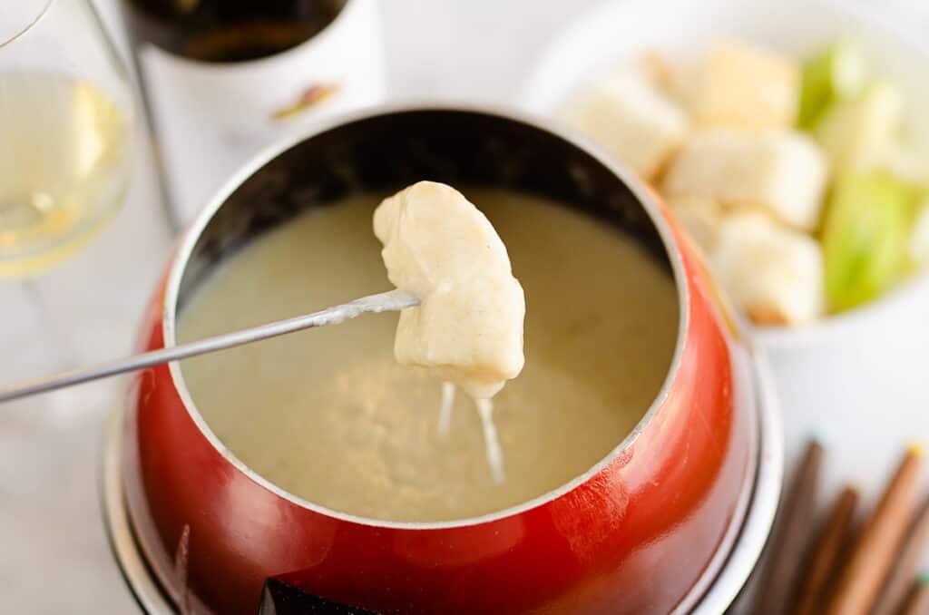 piece of bread dipped in fondue pot with cheese pull