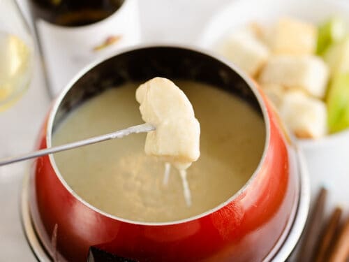 piece of bread dipped in fondue pot with cheese pull