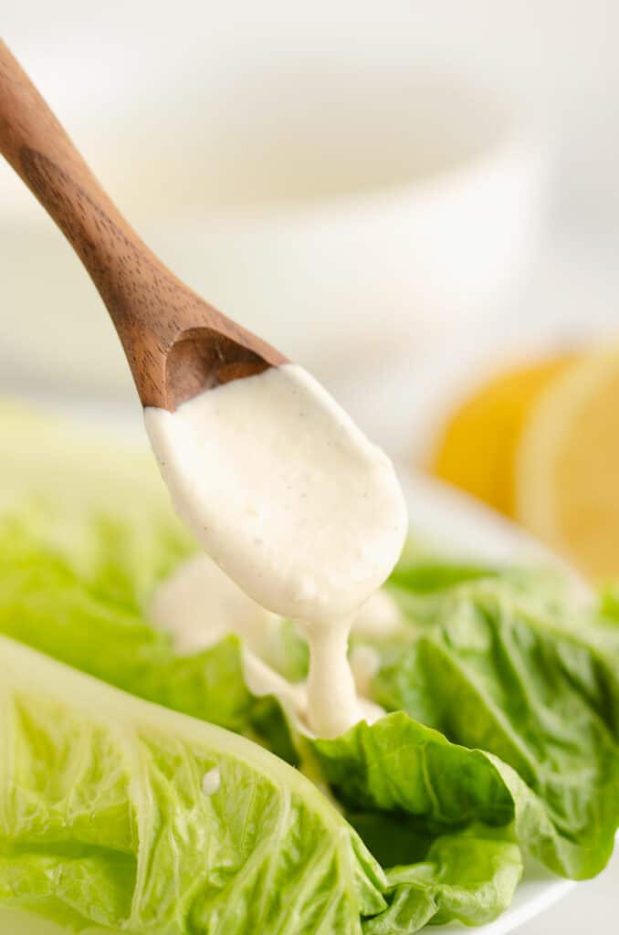 caesar dressing on wooden spoon pouring over romaine lettuce