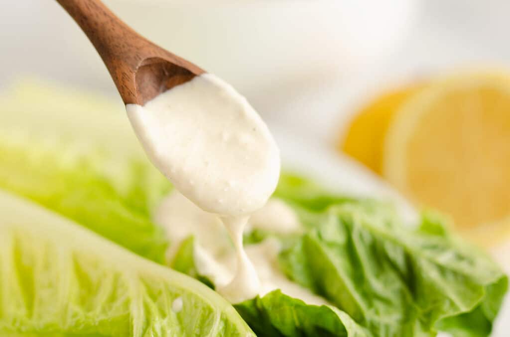 caesar dressing on wooden spoon drizzled over greens