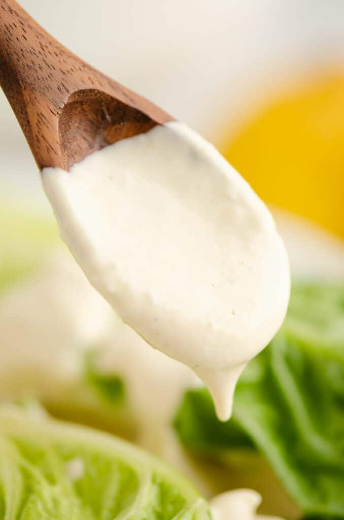 greek yogurt caesar dressing dripping from wooden spoon