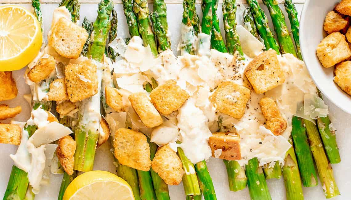 roasted Caesar asparagus on white serving platter with lemon and a bowl of croutons
