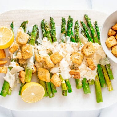 roasted Caesar asparagus on white serving platter with lemon and a bowl of croutons