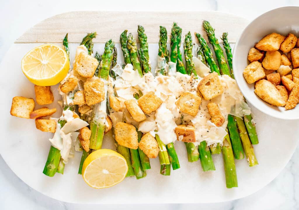 roasted Caesar asparagus on white serving platter with lemon and a bowl of croutons