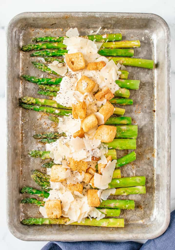 roasted asparagus on baking sheet with Caesar dressing, Parmesan and croutons