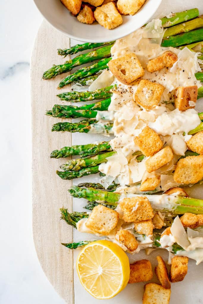 roasted asparagus on white serving platter topped with Caesar dressing and croutons