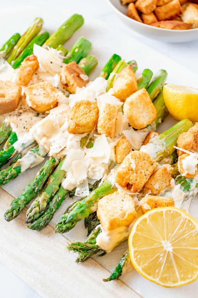 roasted Caesar asparagus on white serving platter with lemons and croutons