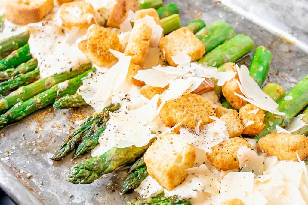 roasted asparagus on baking sheet with Caesar dressing, Parmesan and croutons