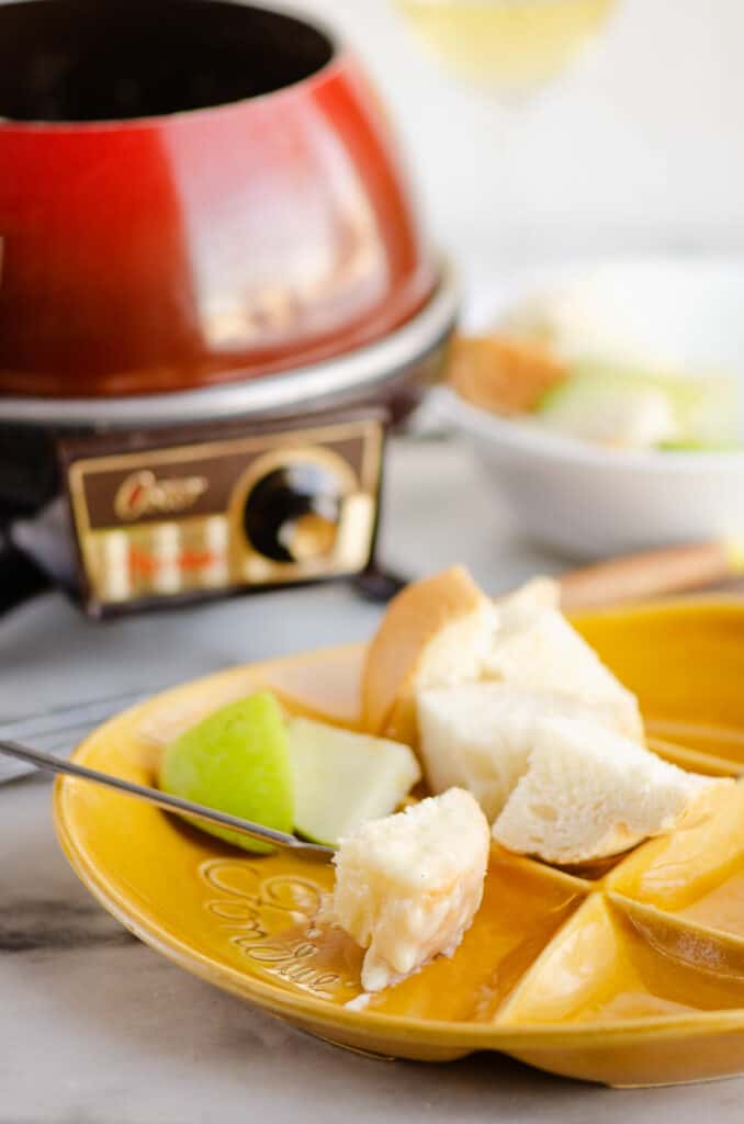 poppy red fondue pot on table with fondue plate with apples and bread dipped in cheese