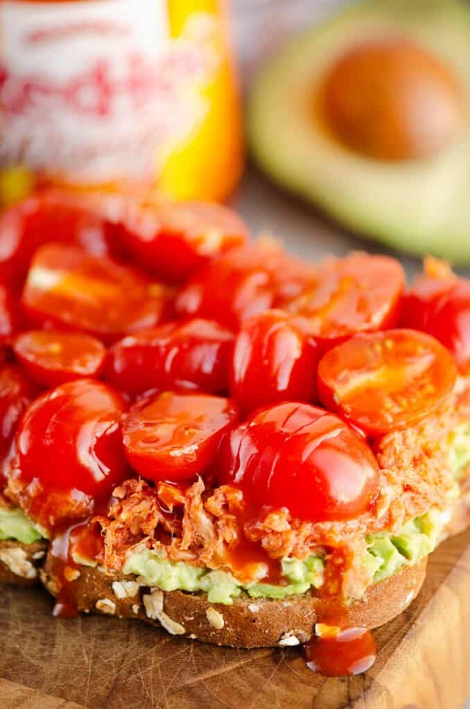 Buffalo Tuna Avocado Toast on cutting board with hot sauce