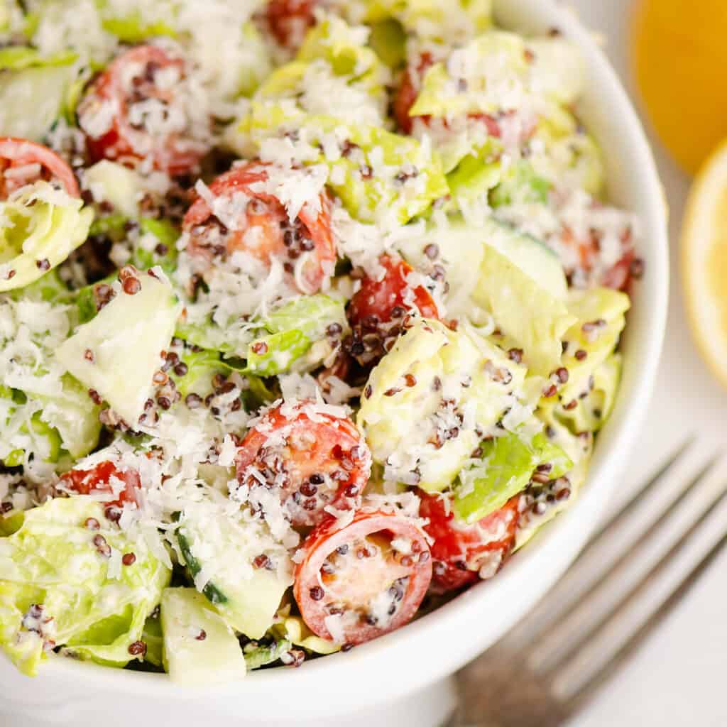 chopped vegetable caesar salad in white bowl with lemon