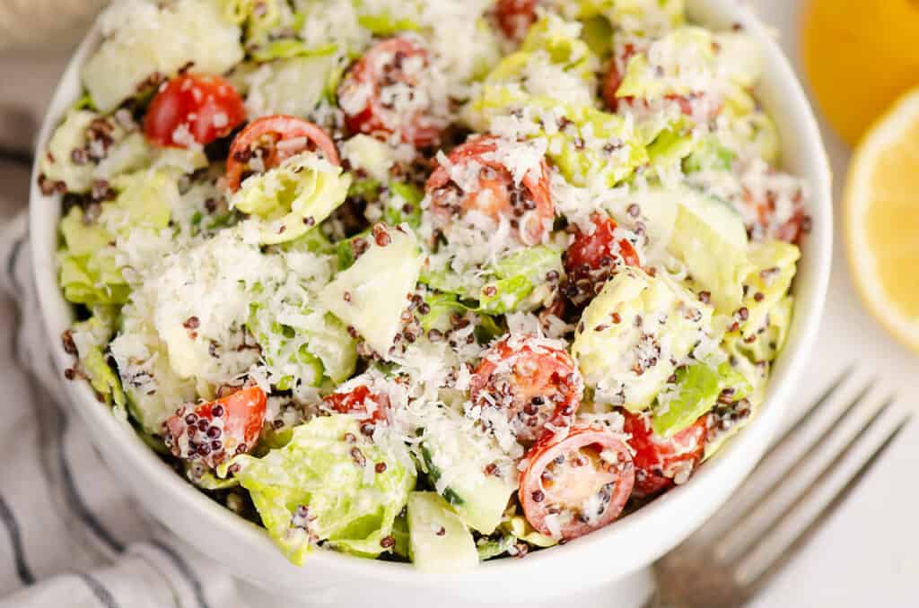 vegetable caesar salad tossed in bowl on table with fork