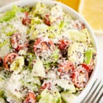 chopped vegetable caesar salad in white bowl with lemon