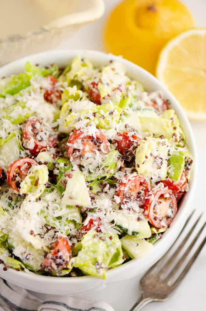 chopped vegetable caesar salad in white bowl with lemon