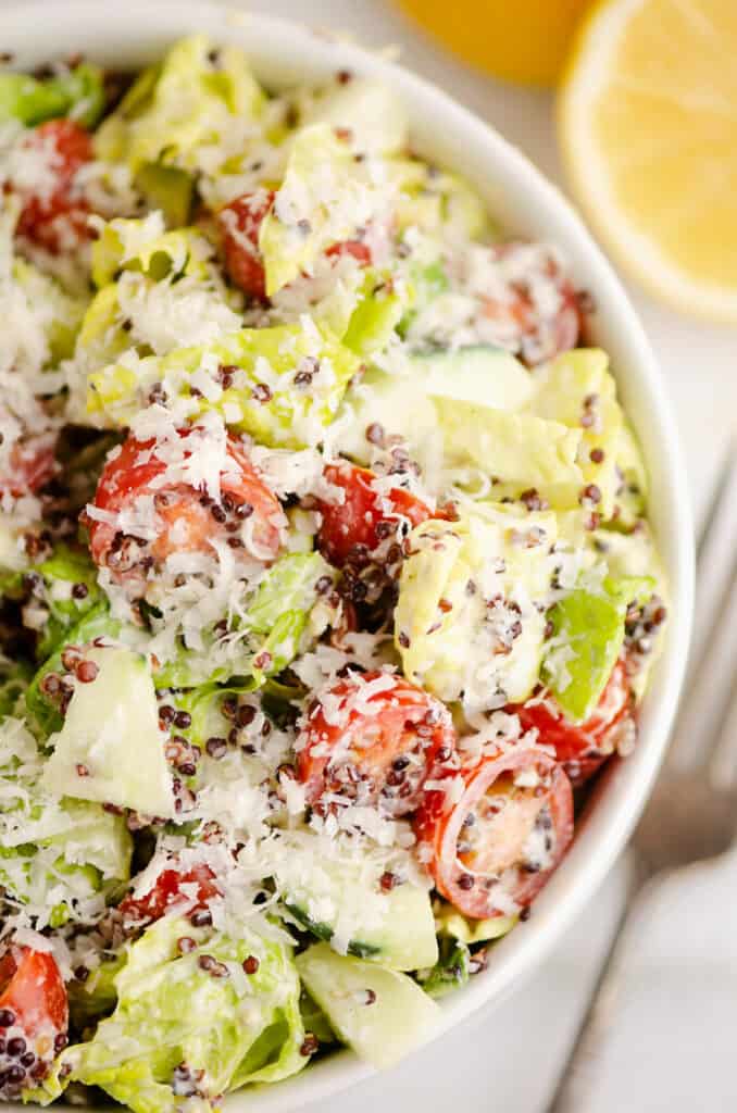 chopped vegetable caesar salad tossed with quinoa in bowl on table with lemon