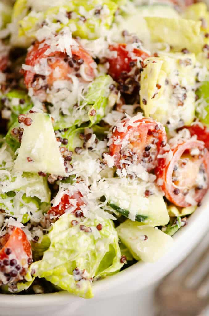 chopped vegetable caesar salad tossed with quinoa in white bowl