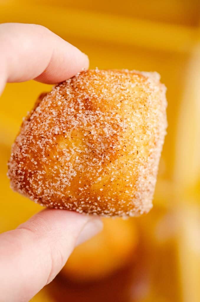 cinnamon sugar biscuit donut hole held over fondue plate