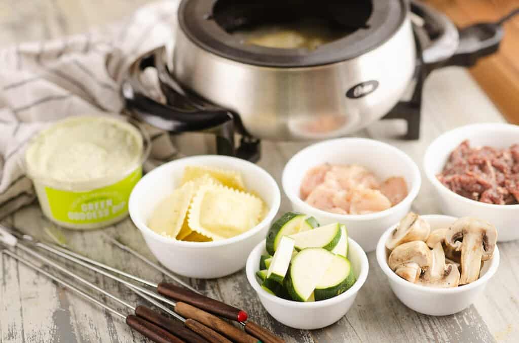 broth fondue pot with vegetables, pasta and meat dippers in bowls