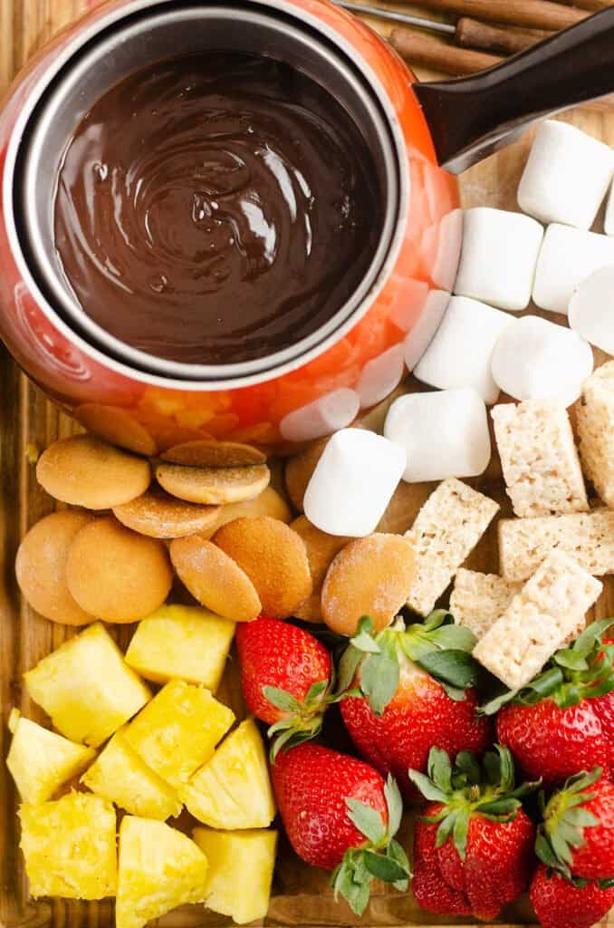 cutting board topped with chocolate fondue and fruit and dessert dippers