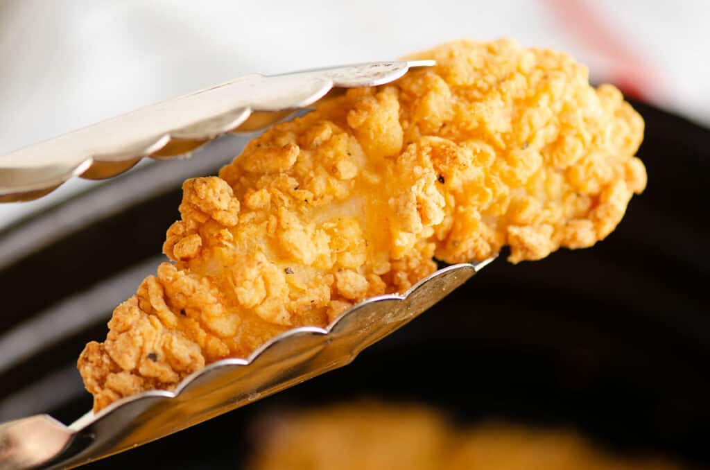 tongs picking up chicken strip from Air Fryer basket