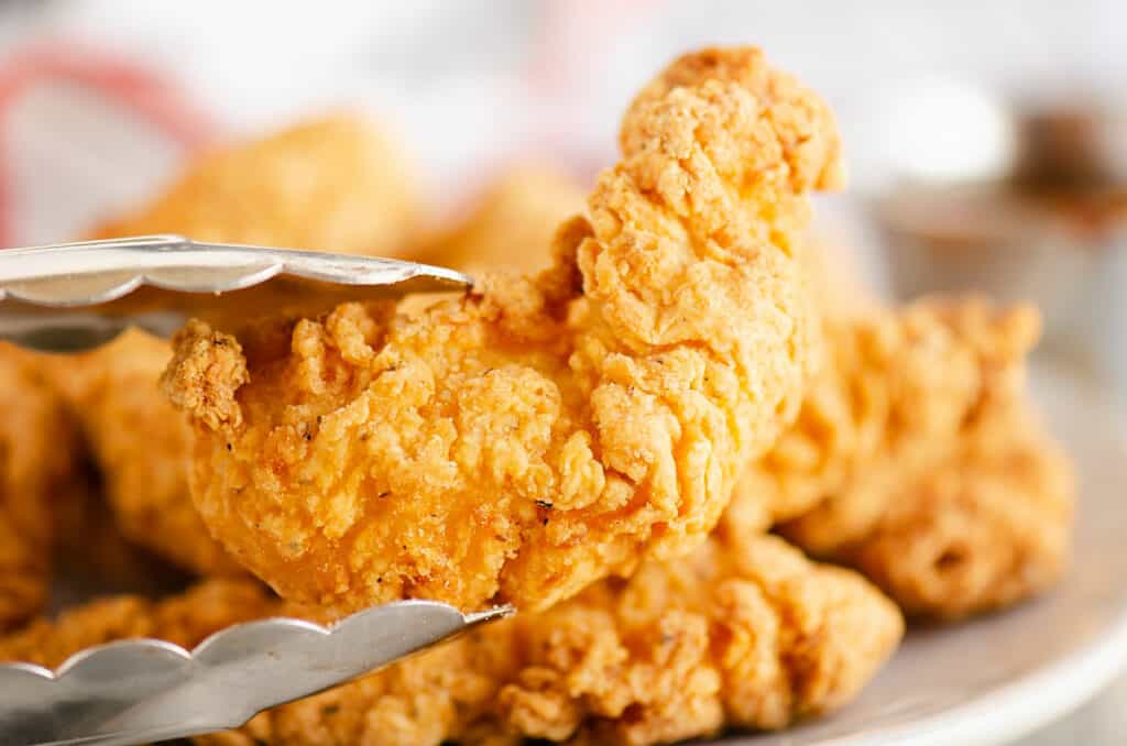 Air Fryer chicken strip being picked up from plate with tong