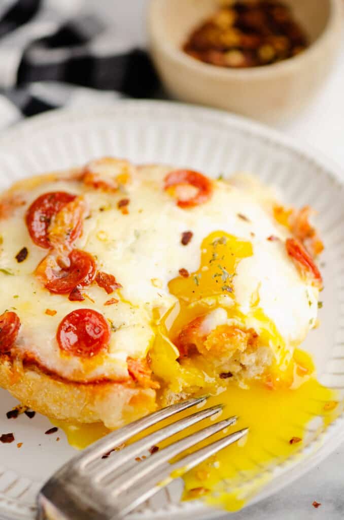 breakfast english muffin pizzas with egg yolk running out on plate with fork