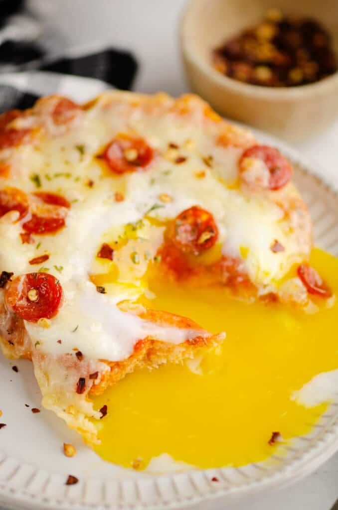 breakfast english muffin pizza with egg yolk running out on plate