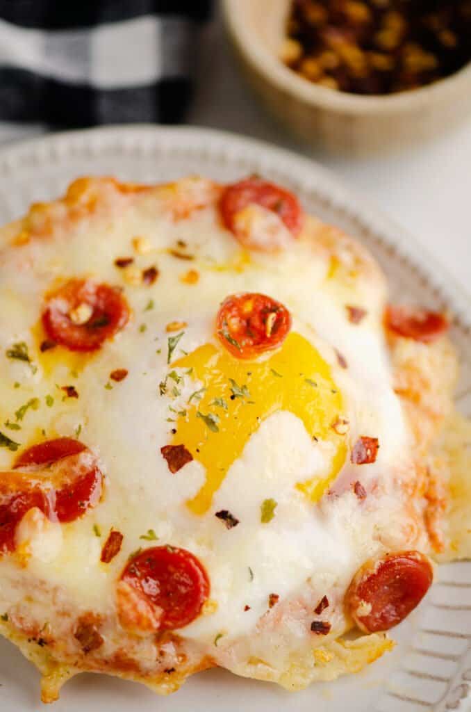 english muffin breakfast pizza on plate with bowl of red pepper flakes