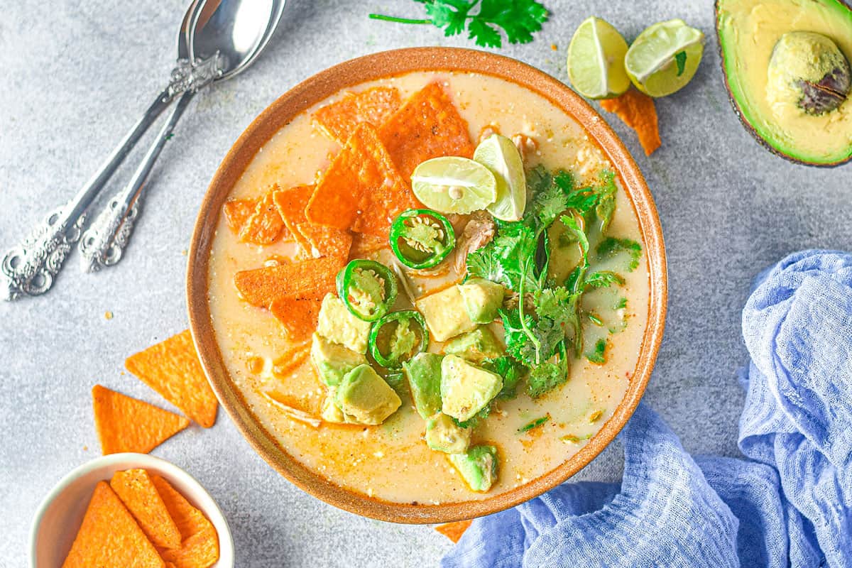 bowl of chicken jalapeno corn soup on table with chips, avocado and blue napkin