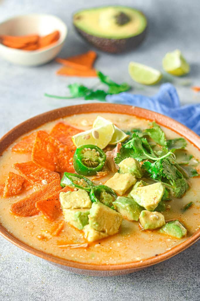 bowl of chicken jalapeno corn soup on table with avocado and chips