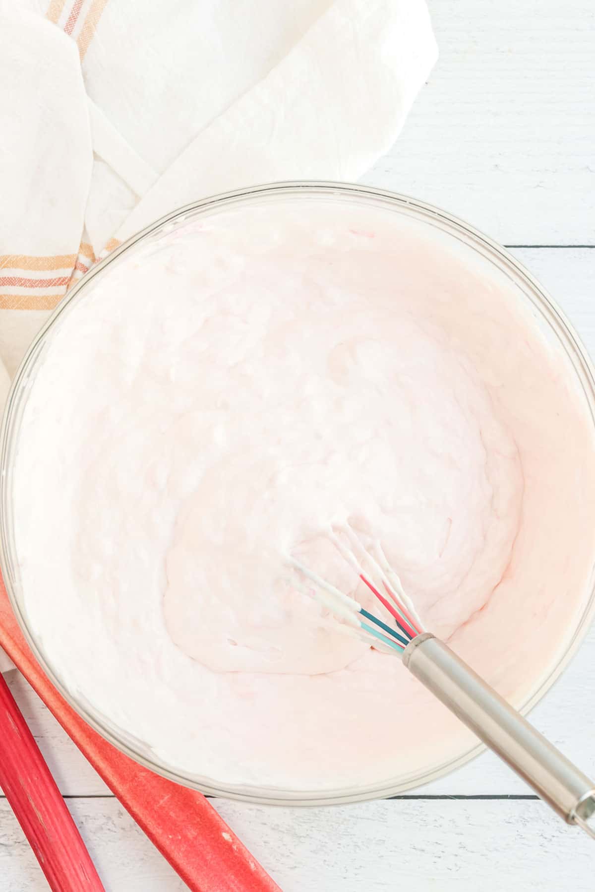 rhubarb and condensed milk mixed in with whipped cream in glass bowl
