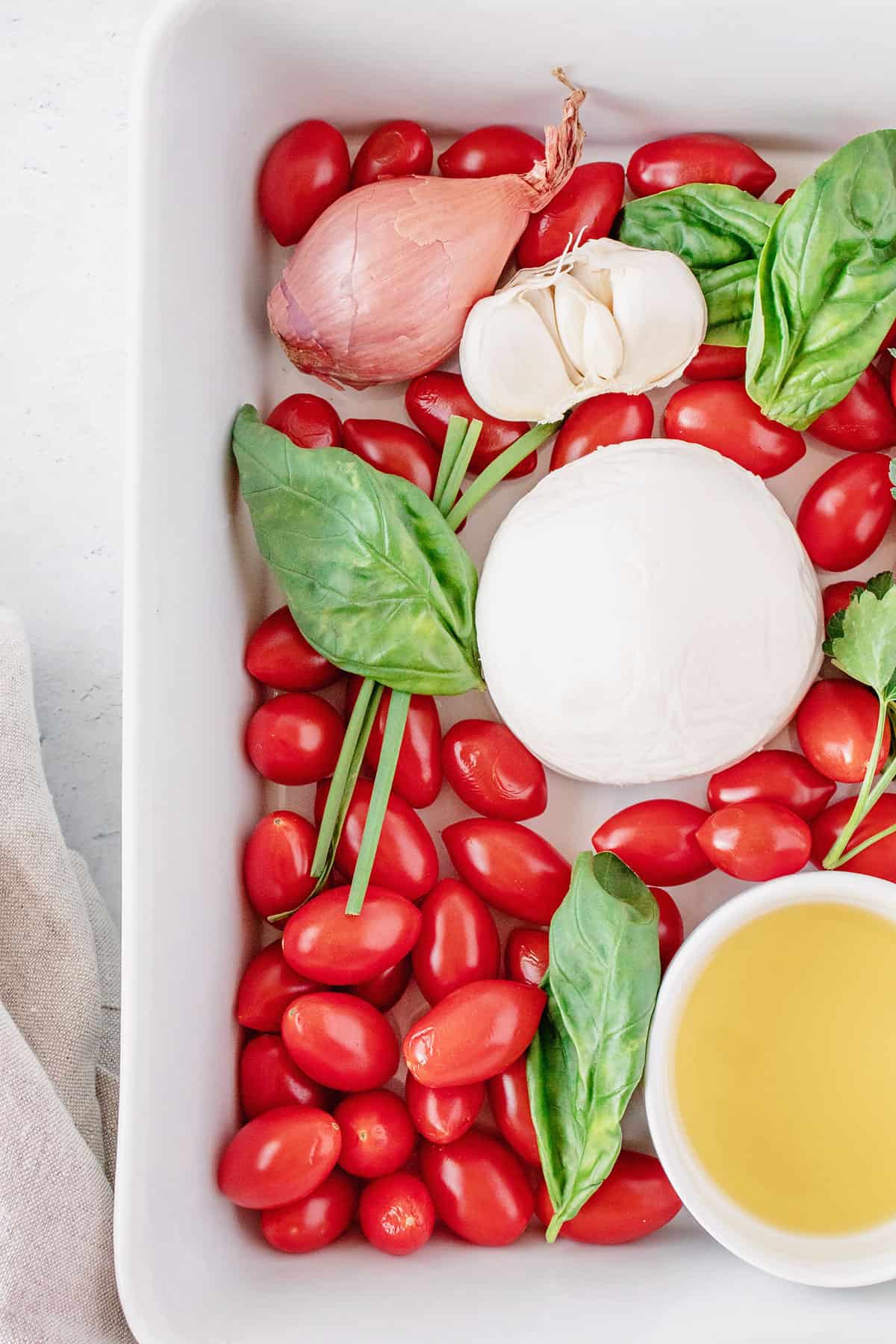 white baking dish with tomatoes, herbs, cheese and olive oil