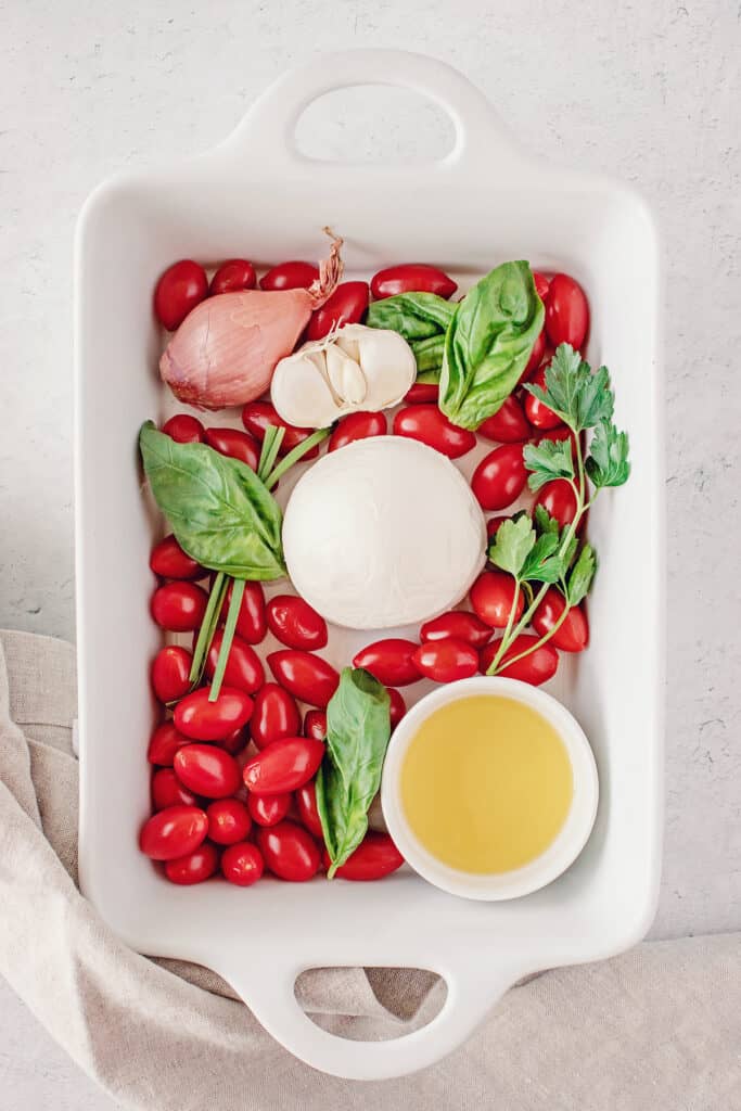 white baking dish with tomatoes, herbs, cheese and olive oil